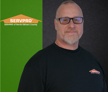 Man smiling at the camera with green and black background and servpro logo
